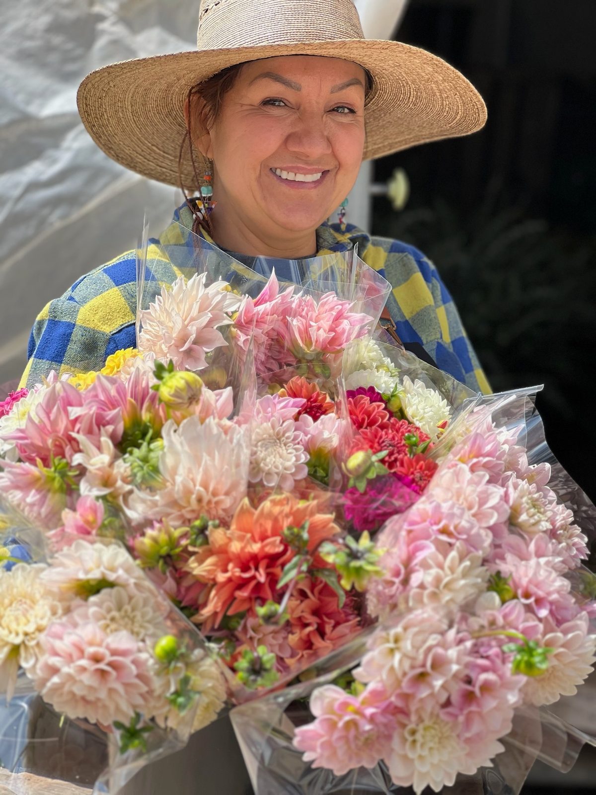 Judith in a straw hat with an armful of wrapped dahlia bouquets at Campesina Flowers