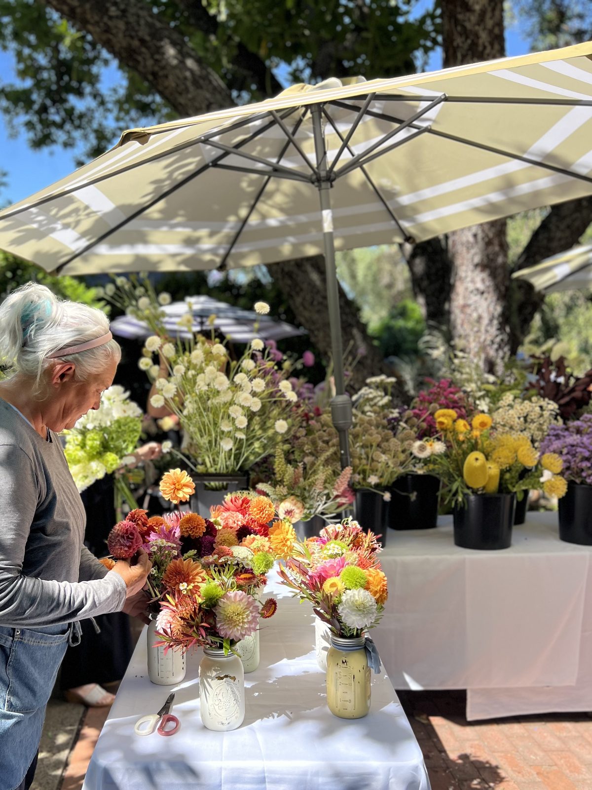 Melissa's flower table under white umbrellas, mason jars of dahlias and strawflowers laid out