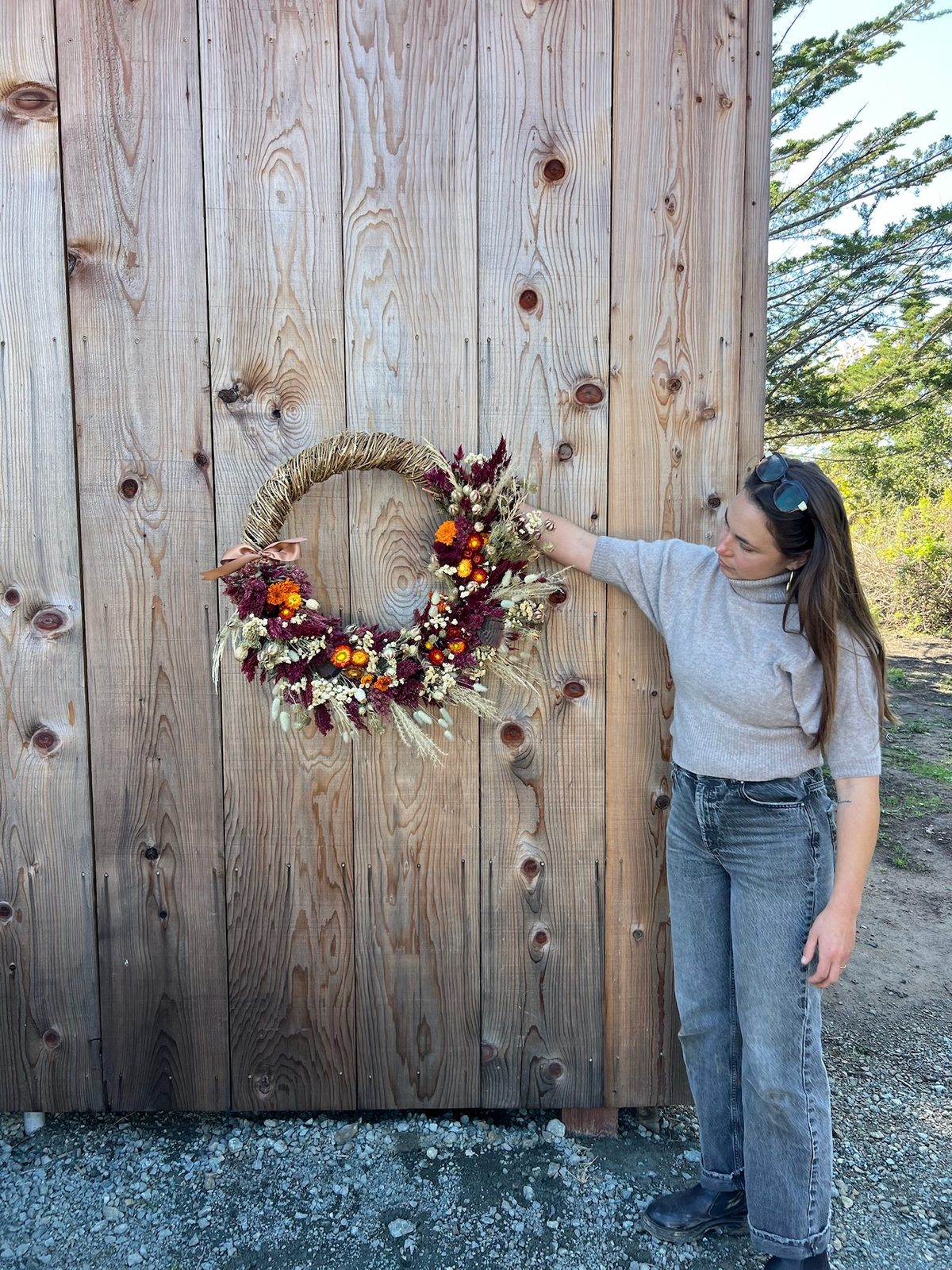 Amelie hanging a dried-flower wreath of strawflower, celosia and bunny tails on a barn wall